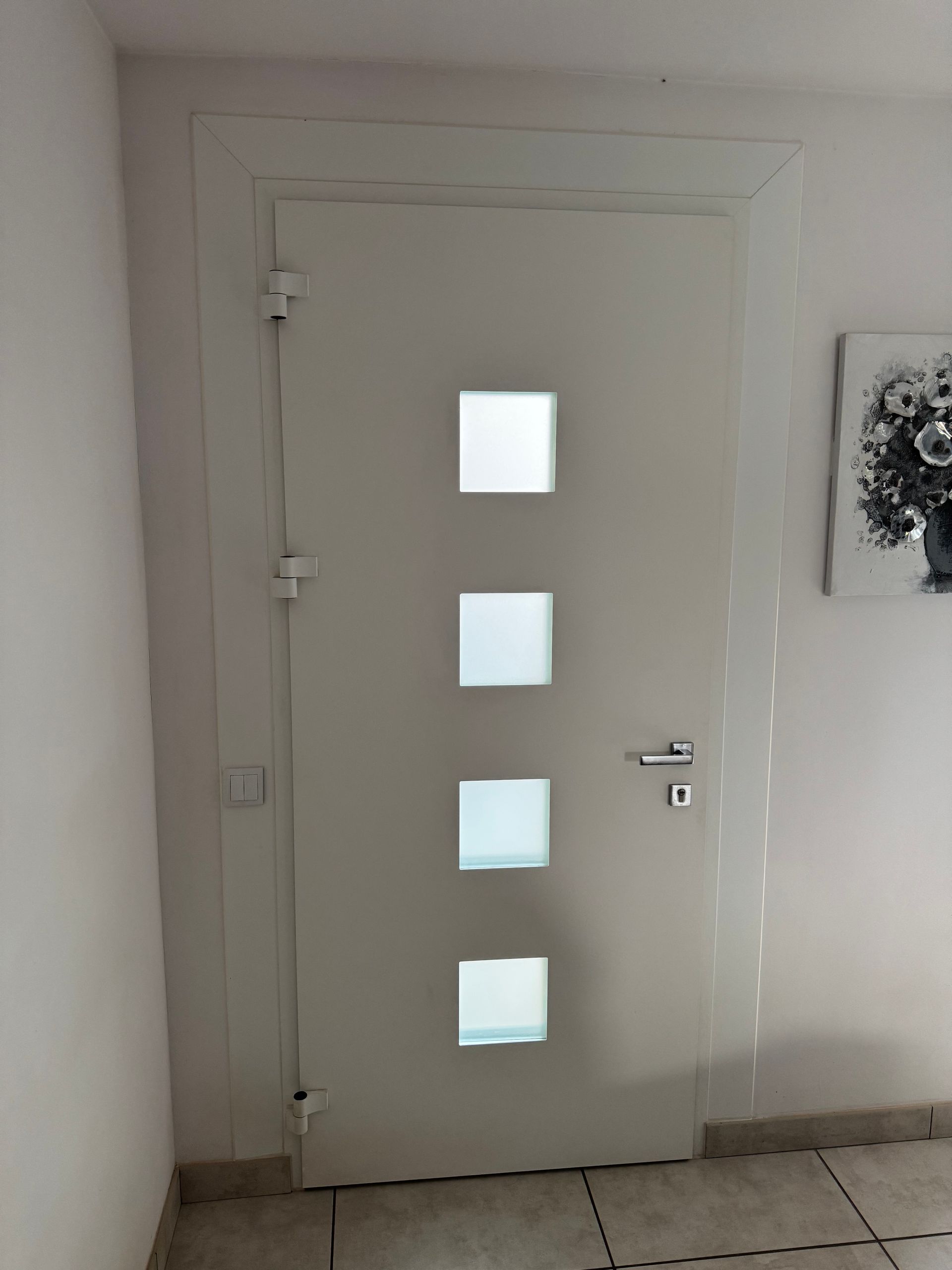 Porte blanche à quatre panneaux de verre carrés, encadrée d'un cadre blanc.