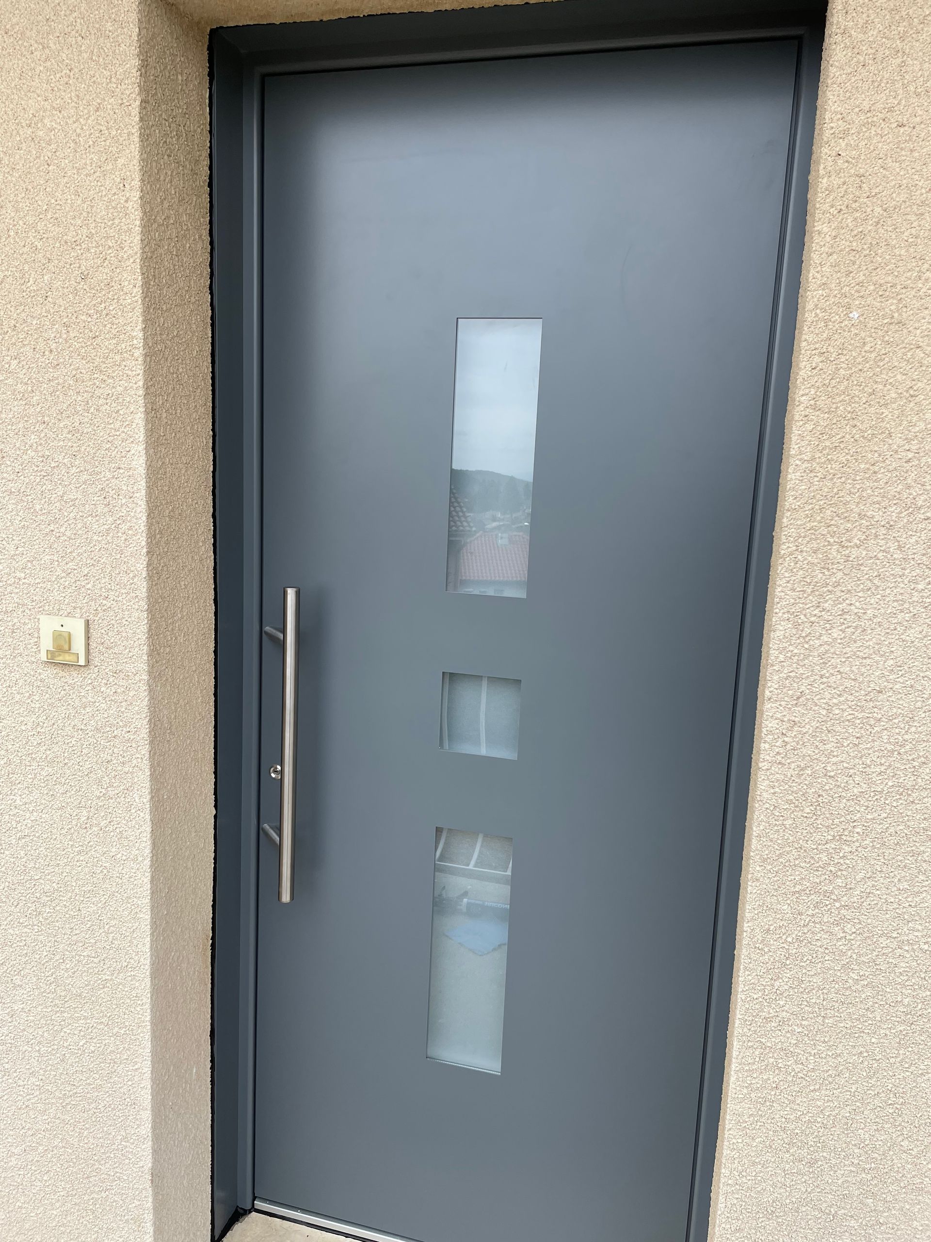 Porte d'entrée grise avec trois fenêtres rectangulaires dépolies.