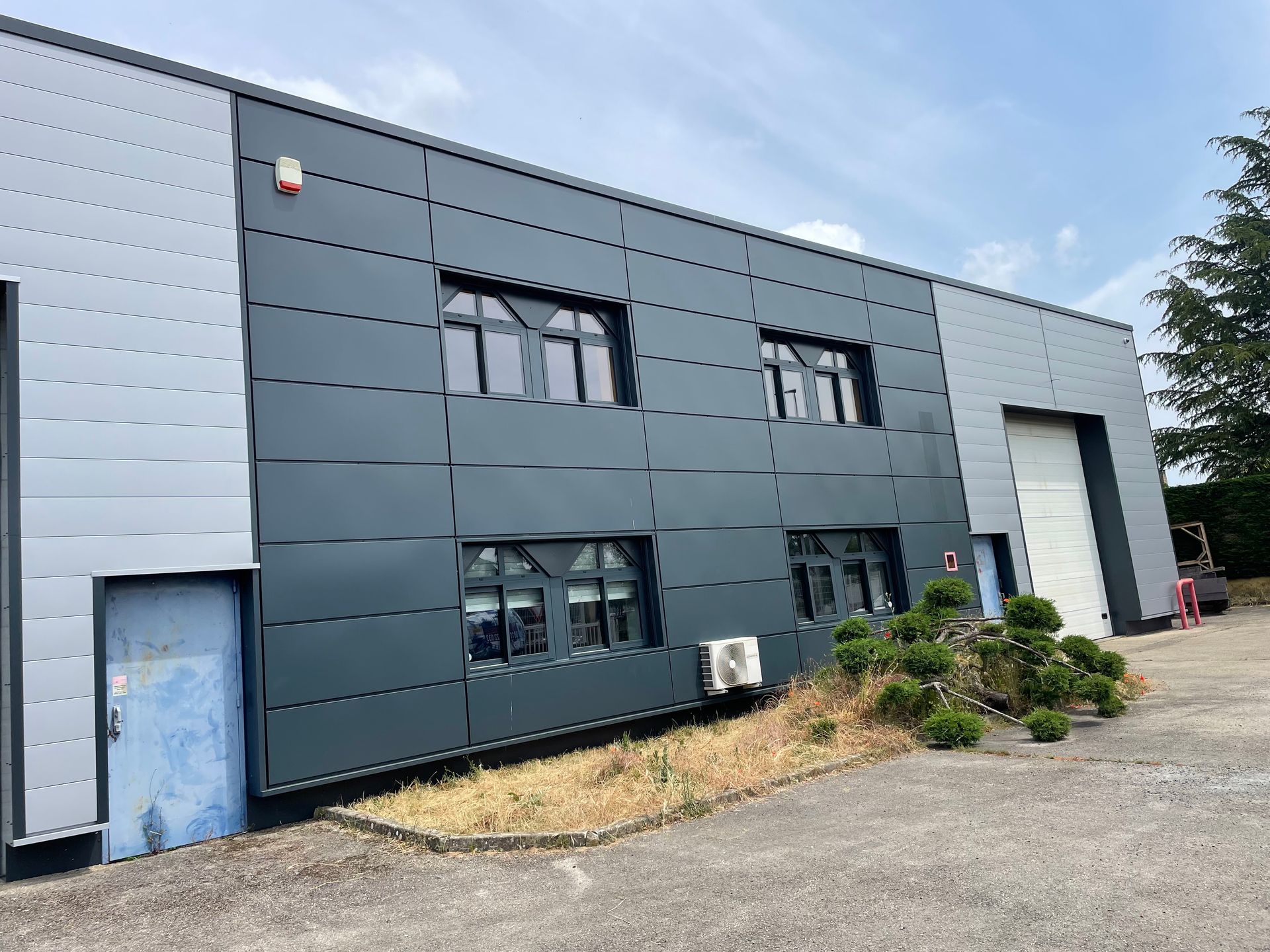 Bâtiment industriel gris foncé et gris clair avec fenêtres.