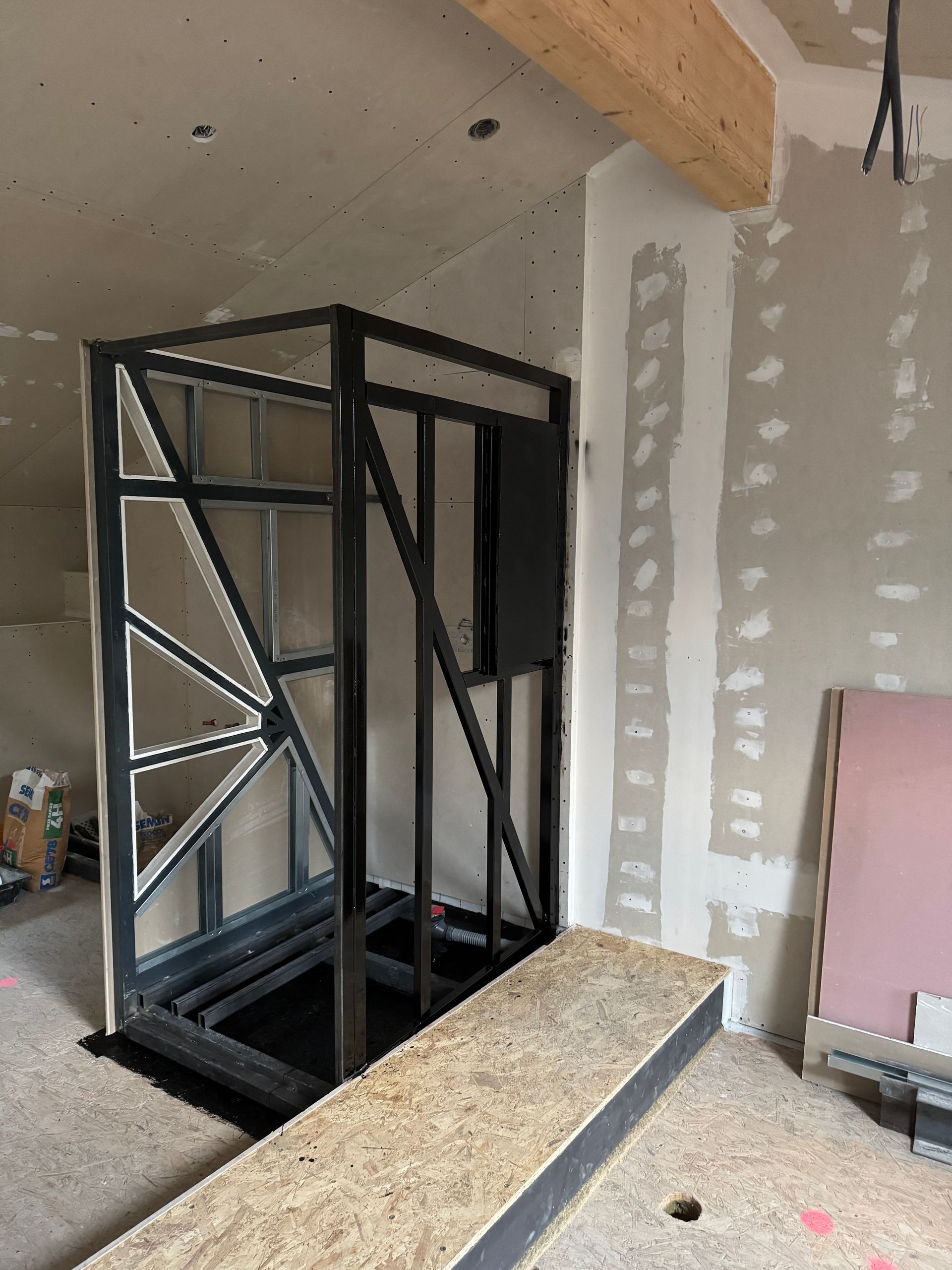 La structure métallique de la cage d'ascenseur est en construction, avec une rampe en bois y menant.