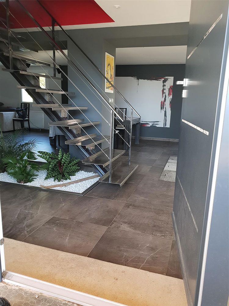 Intérieur : entrée de maison moderne avec escalier, porte grise, art, plantes et sols en marbre.