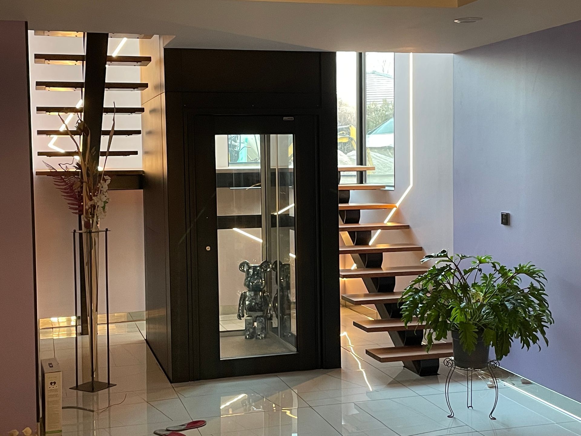 Intérieur de maison moderne avec ascenseur et escalier, comportant des éléments en verre, en métal et en bois.