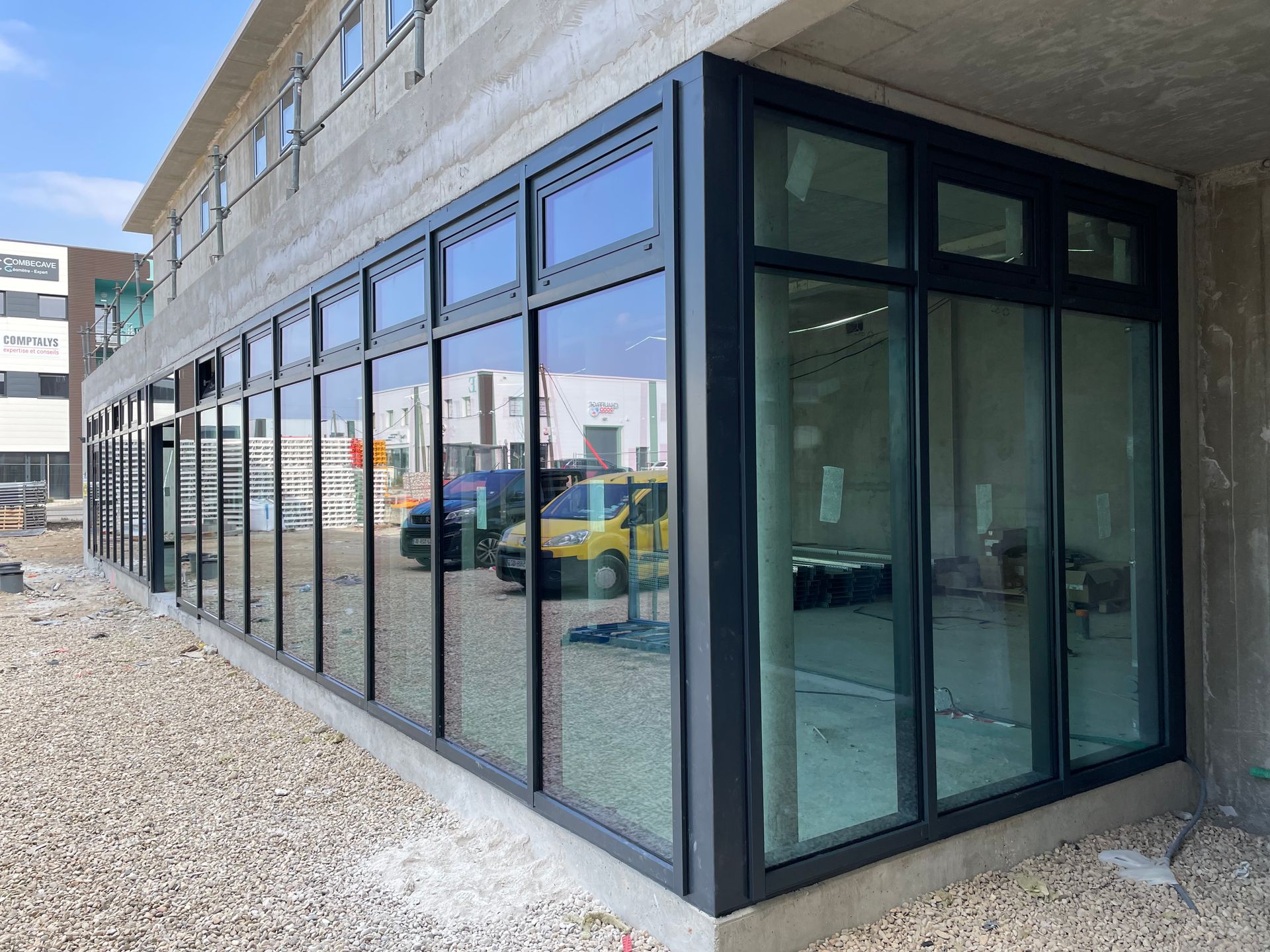 Extérieur d'un bâtiment avec de grandes fenêtres et des cadres noirs, en construction.