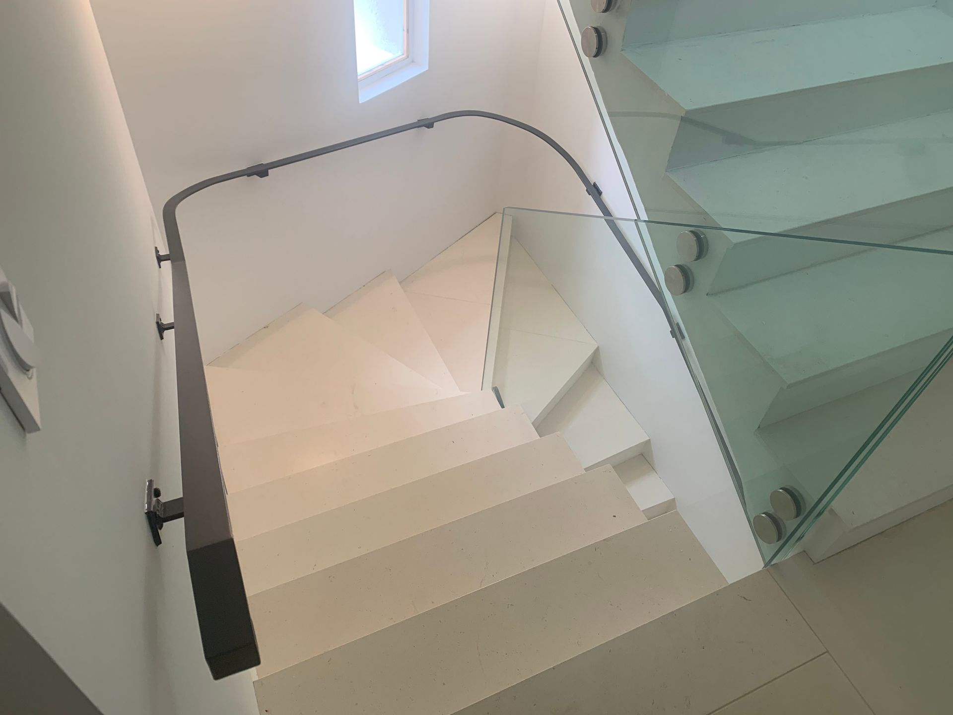 Escalier avec marches blanches, rampe en verre et main courante foncée. Vue intérieure.