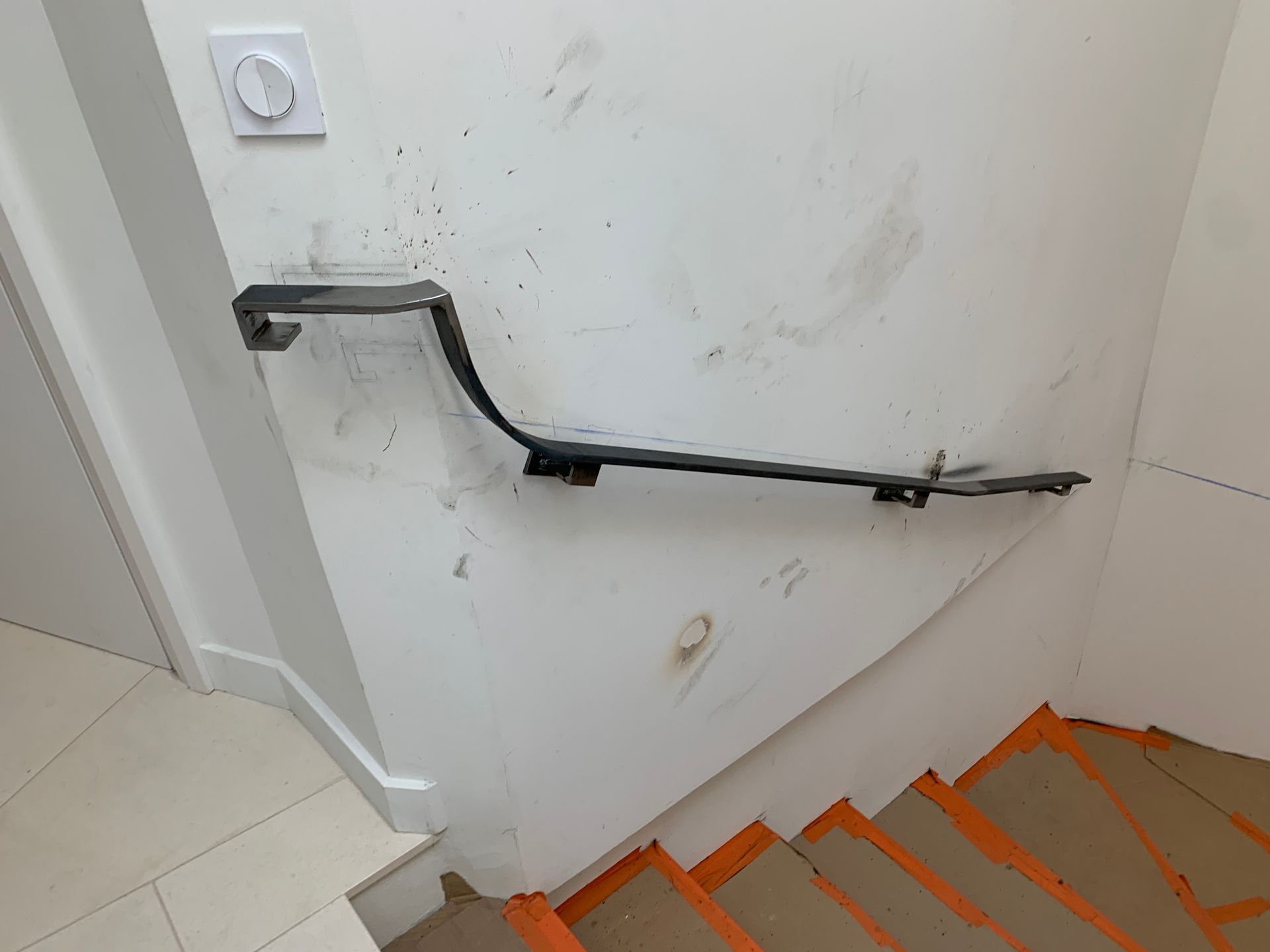 Main courante sur un mur blanc au-dessus d'un escalier recouvert d'orange.
