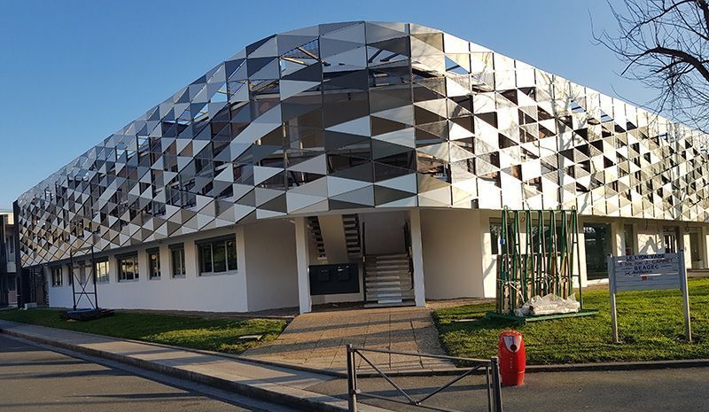 Bâtiment moderne avec façade réfléchissante et géométrique sous un ciel bleu.