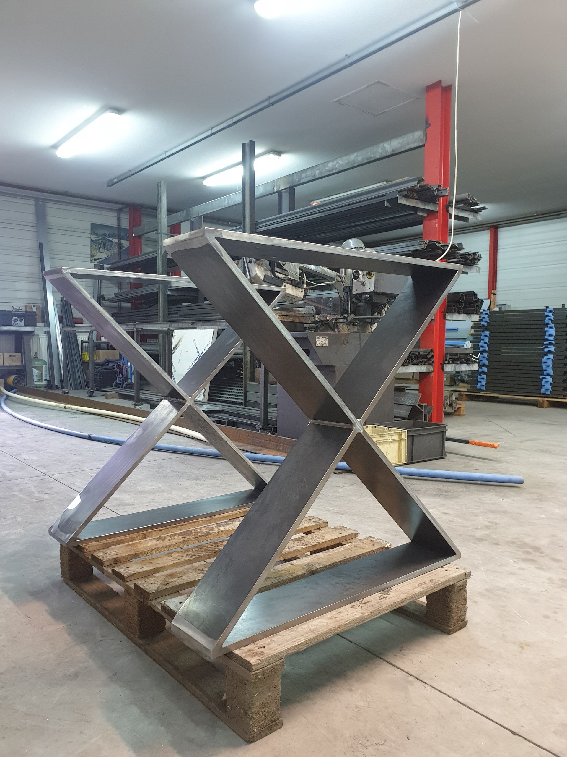 Piètement de table en métal en forme de X sur une palette en bois, à l'intérieur d'un atelier.