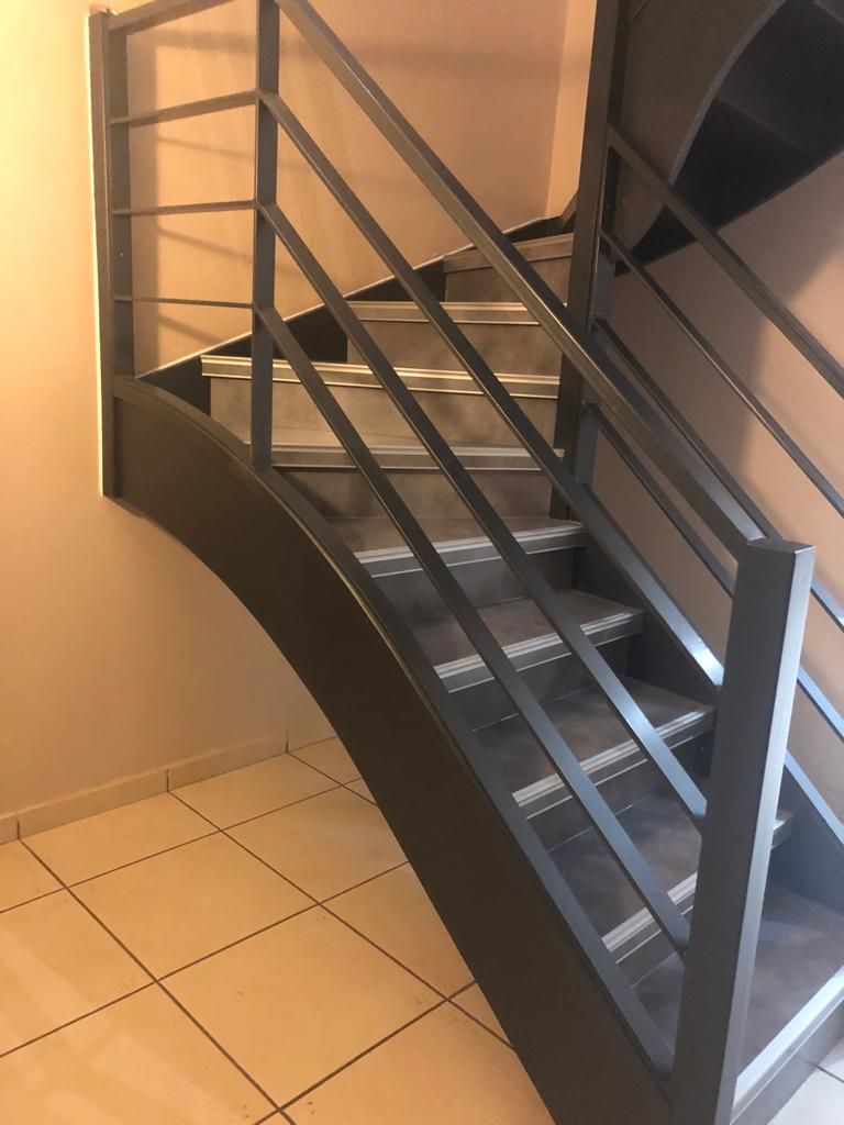 Escalier avec rampes et marches en métal foncé contre murs et sol beiges, montant.