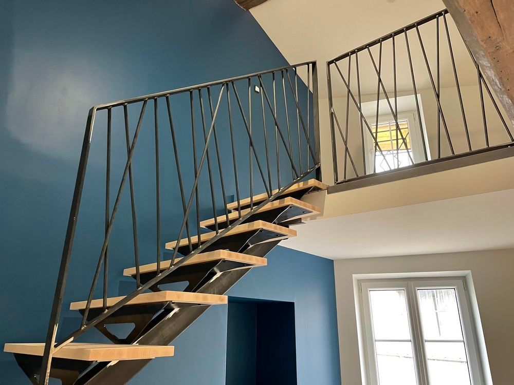 Escalier en bois avec rampe en métal noir sur fond de murs bleus et beiges.