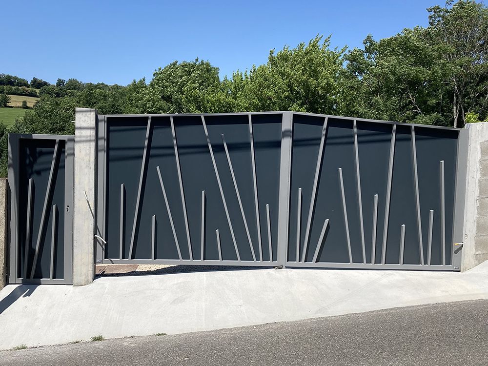 Portail en métal gris avec barreaux argentés en diagonale, posé sur une allée en béton avec des arbres en arrière-plan.