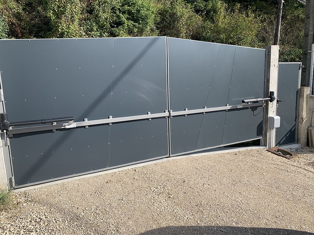 Portail d'allée automatique en métal gris, fermé, allée en gravier, extérieur.