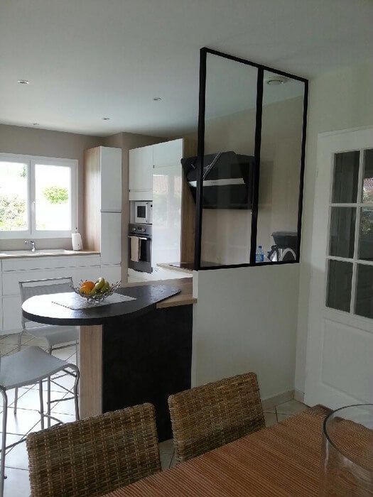 Cuisine avec cloison vitrée à cadre noir; îlot avec bar, table avec chaises et fenêtre.