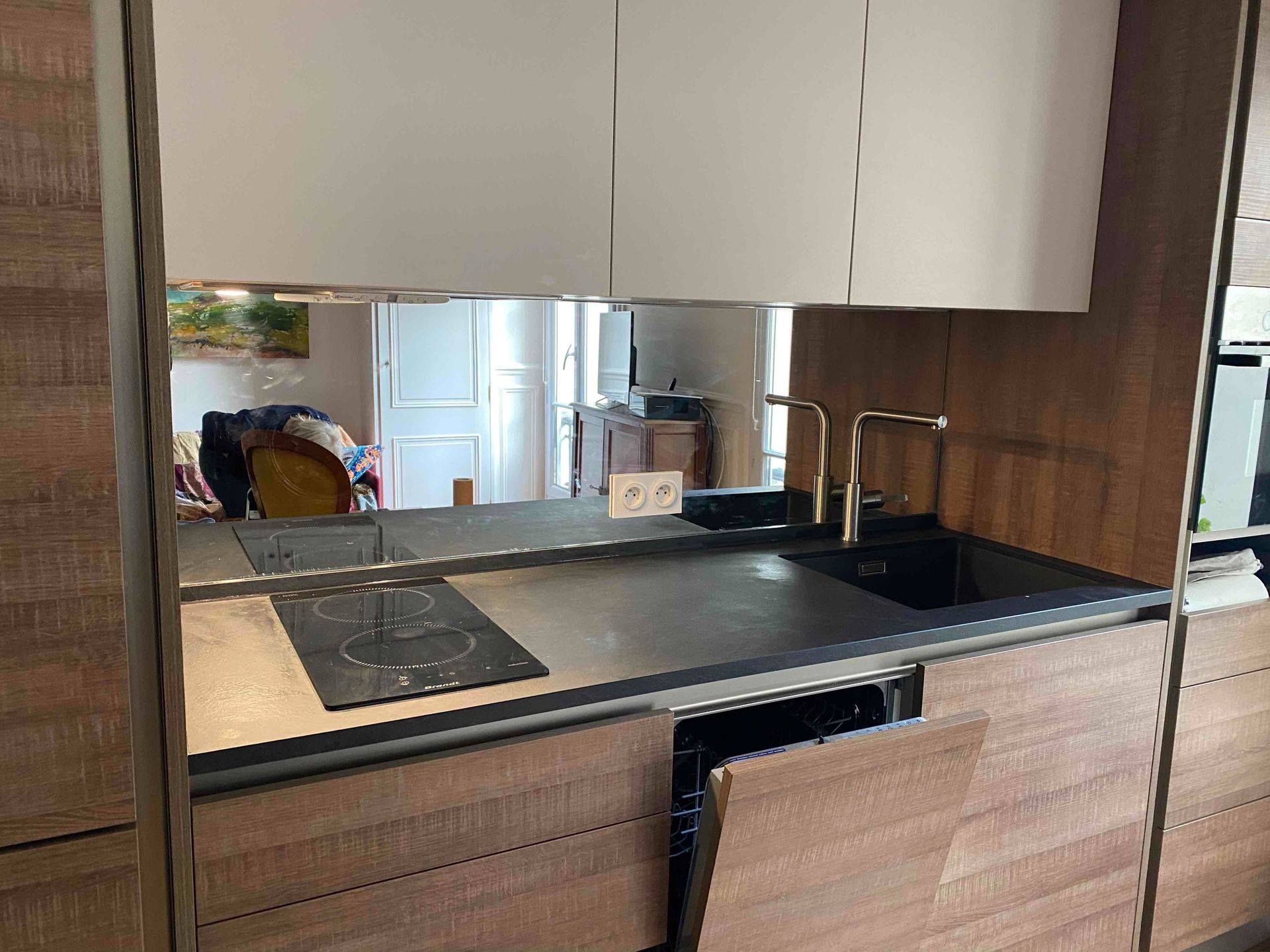 Cuisine moderne avec placards en bois, plan de travail noir, évier, plaque de cuisson et robinet doré, avec lave-vaisselle ouvert.