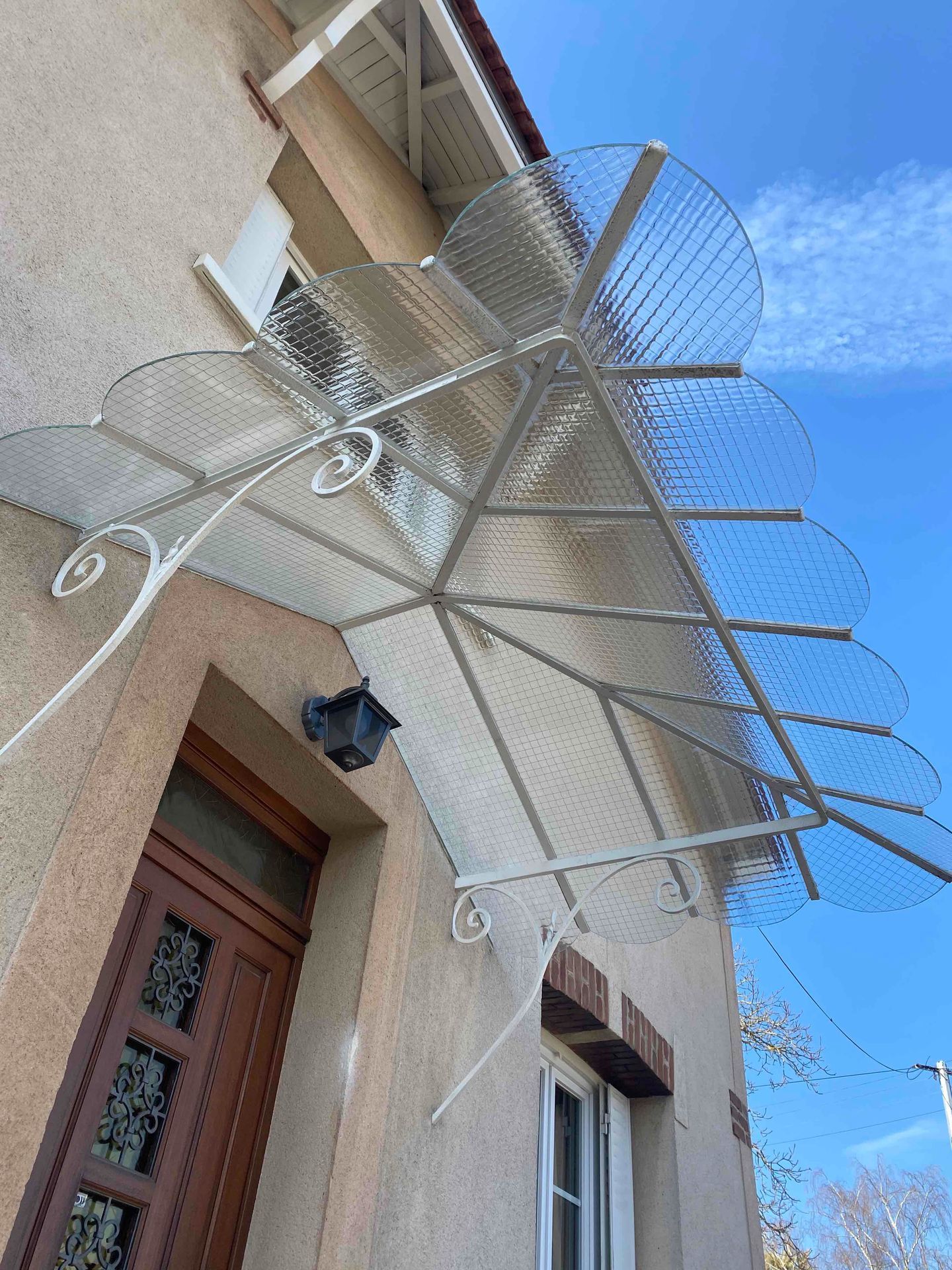 Métal blanc et marquise transparente recouvrent une porte et une fenêtre en bois sur un bâtiment beige.