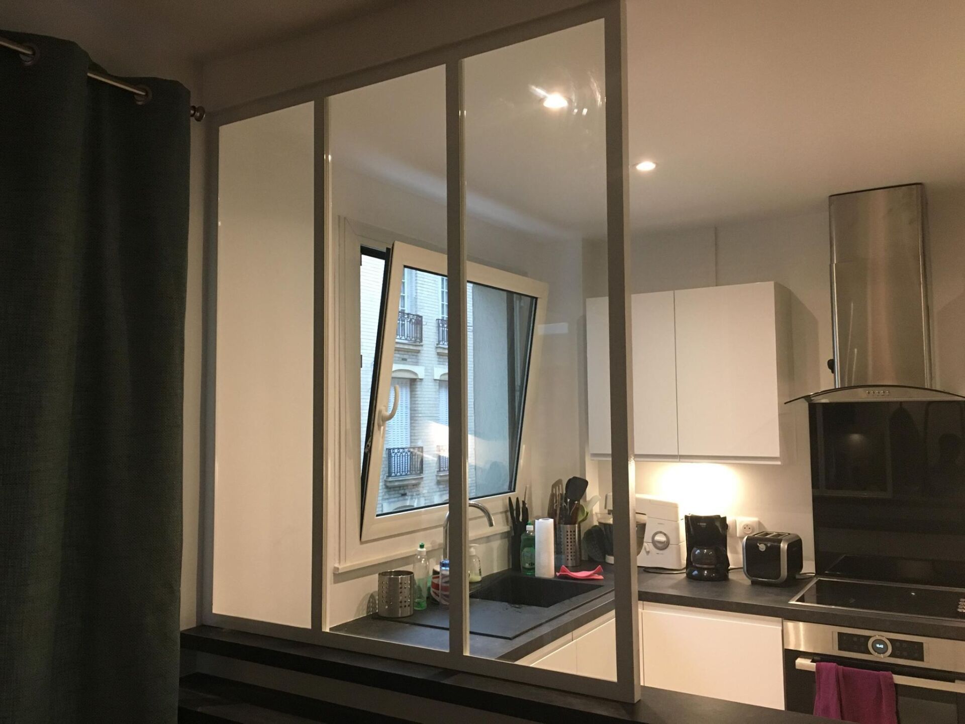 Une cuisine avec une cloison vitrée et une fenêtre, avec des placards et des appareils électroménagers blancs.