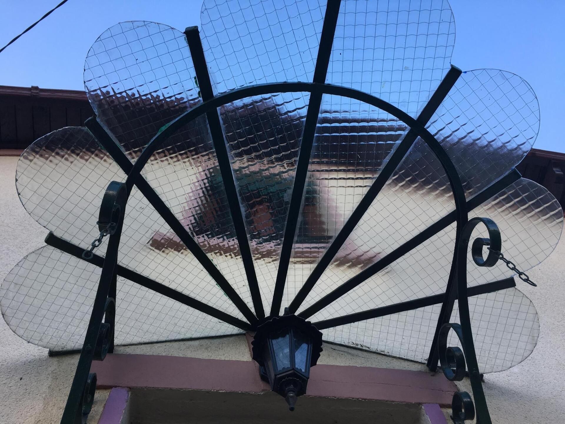 Marquise en fer forgé noir et verre transparent au-dessus d'une porte, en forme de fleur.