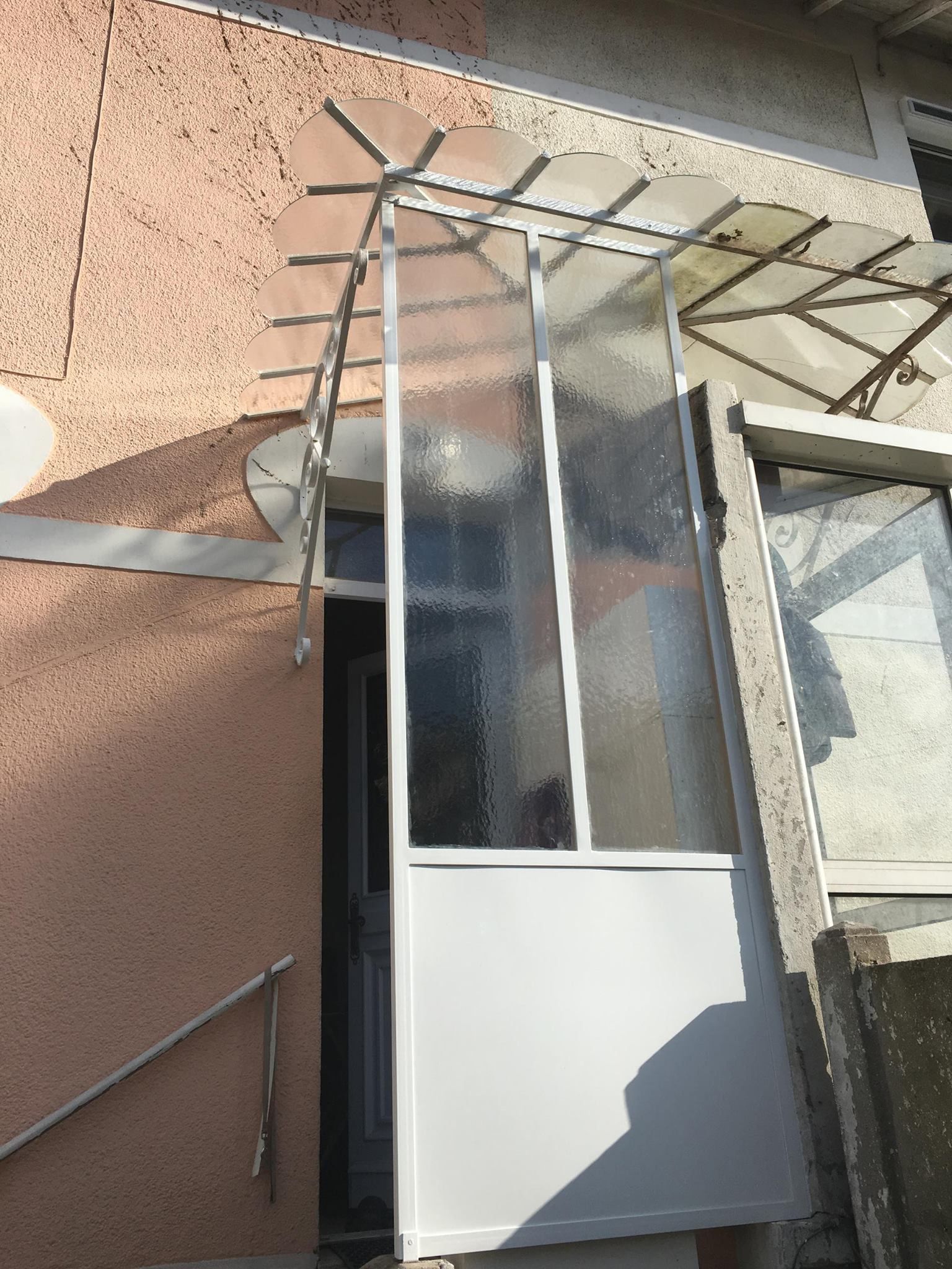 Porte blanche et vitrée avec une marquise translucide, intégrée dans un mur en stuc couleur pêche.