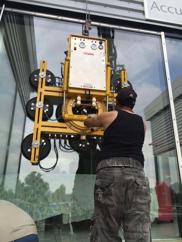 Un homme utilise un dispositif de levage monté sur une grue pour installer une grande vitre dans un bâtiment.