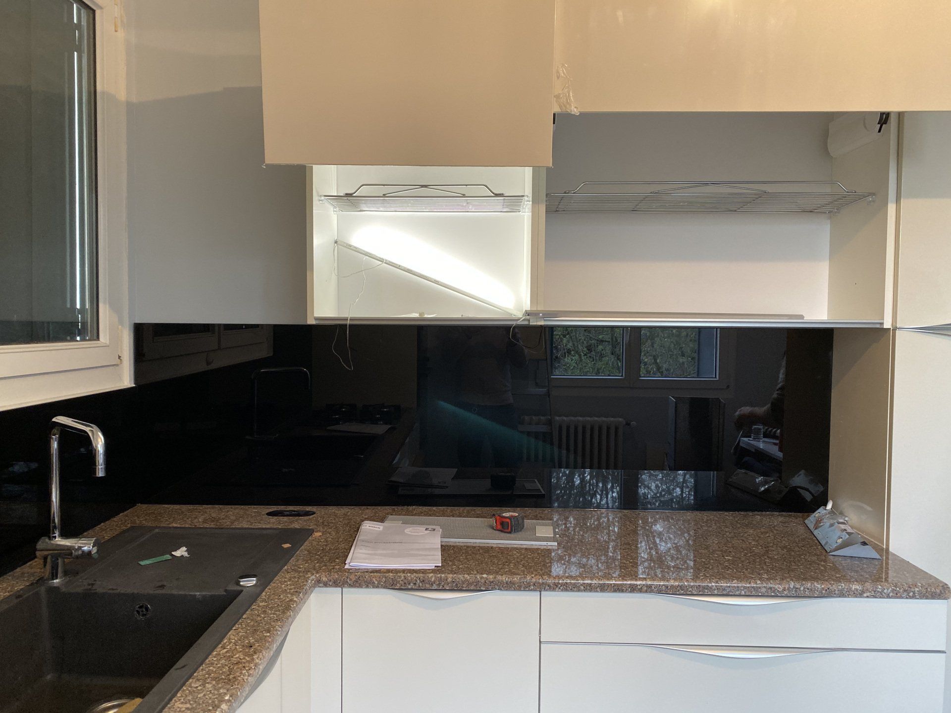 Cuisine avec crédence noire, armoires blanches, comptoir en granit et évier en acier inoxydable.