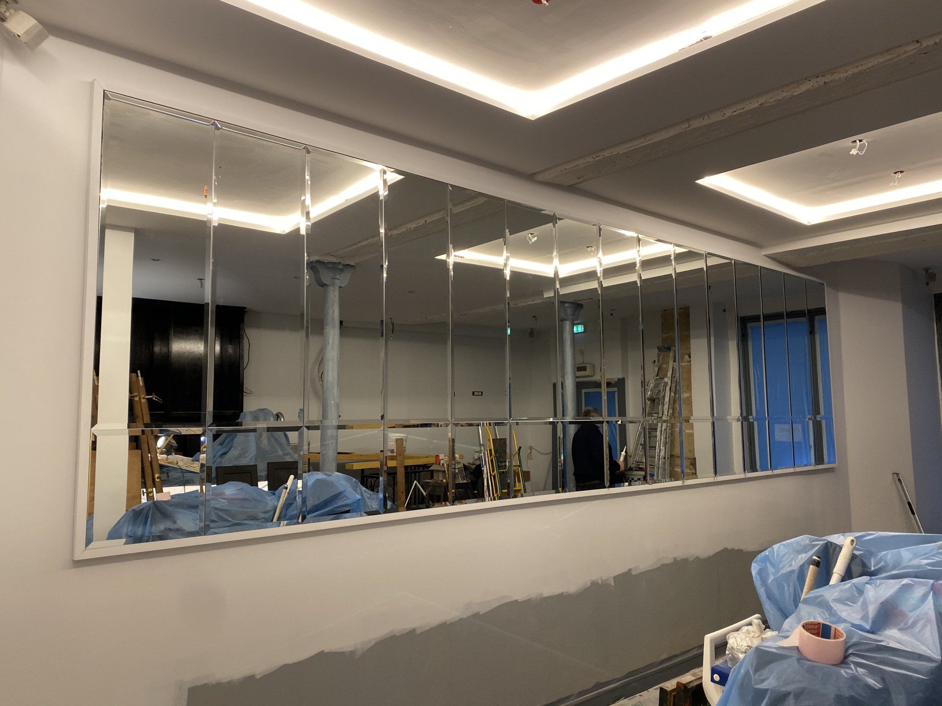 Grand mur de miroirs reflétant une pièce en construction avec des matériaux de construction.