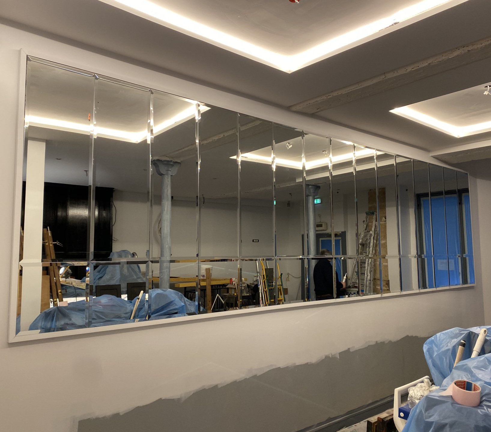 Grand miroir mural composé de panneaux rectangulaires, reflétant une pièce en construction.