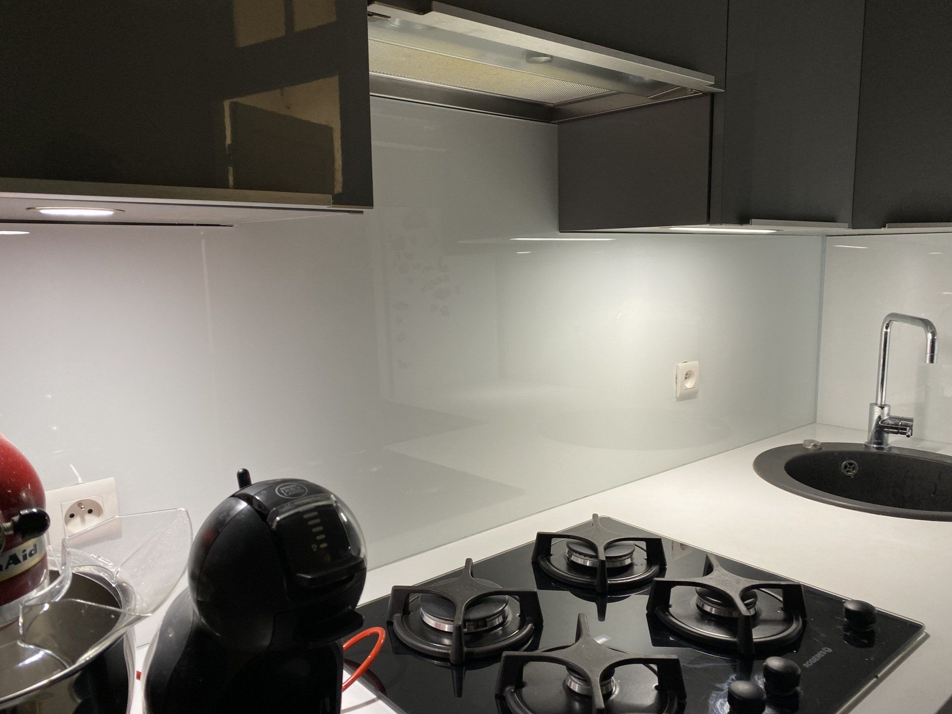 Cuisine moderne avec plaque de cuisson noire, crédence blanche et hotte en acier inoxydable.
