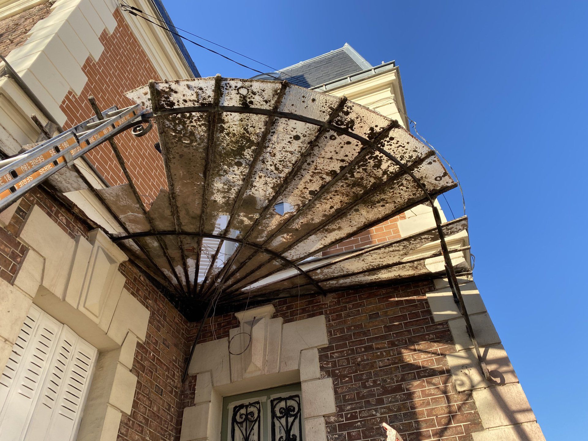 Bâtiment en briques avec une marquise en métal et en verre au-dessus d'une porte. Une échelle est appuyée contre le bâtiment.