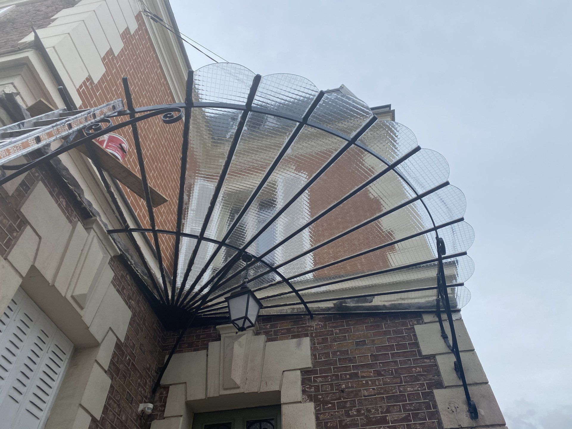 Une marquise décorative en verre et en métal surplombe l'entrée d'un bâtiment, avec une façade en briques et un ciel couvert.