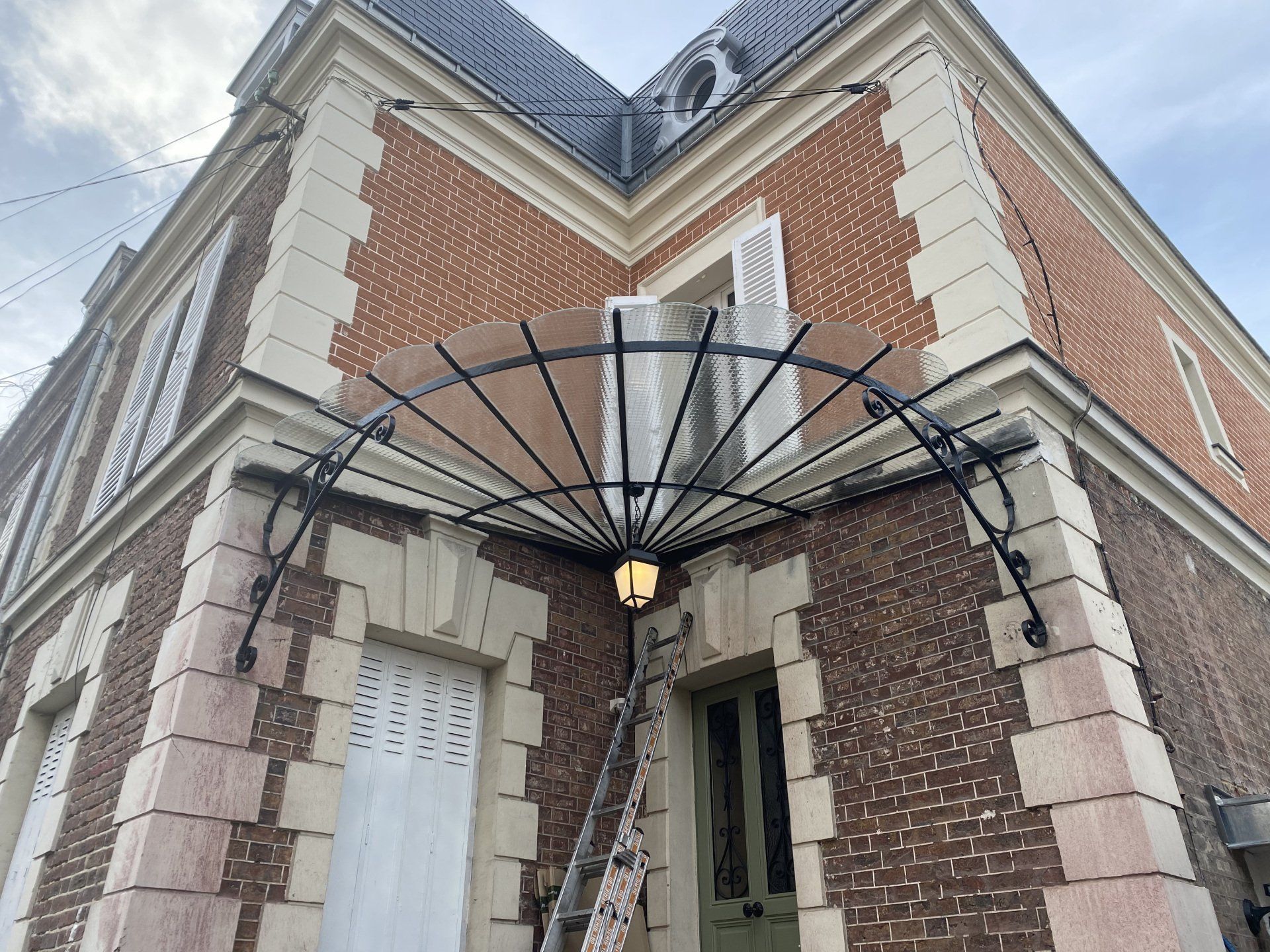 Bâtiment en briques avec une verrière au-dessus d'une porte, des supports en métal noir et une lanterne.