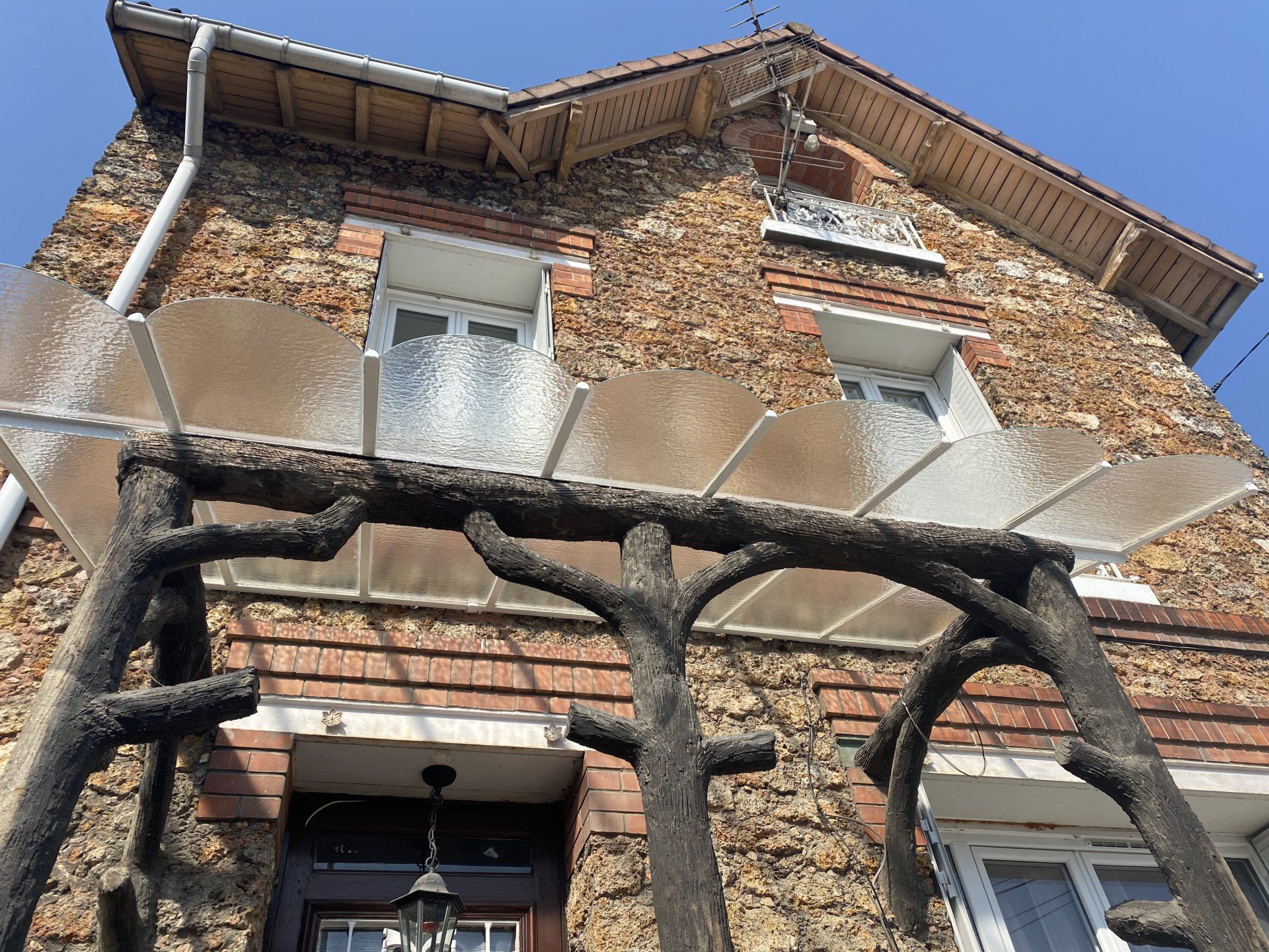 Maison en pierre avec une marquise en verre et des poutres en bois au-dessus de la porte.