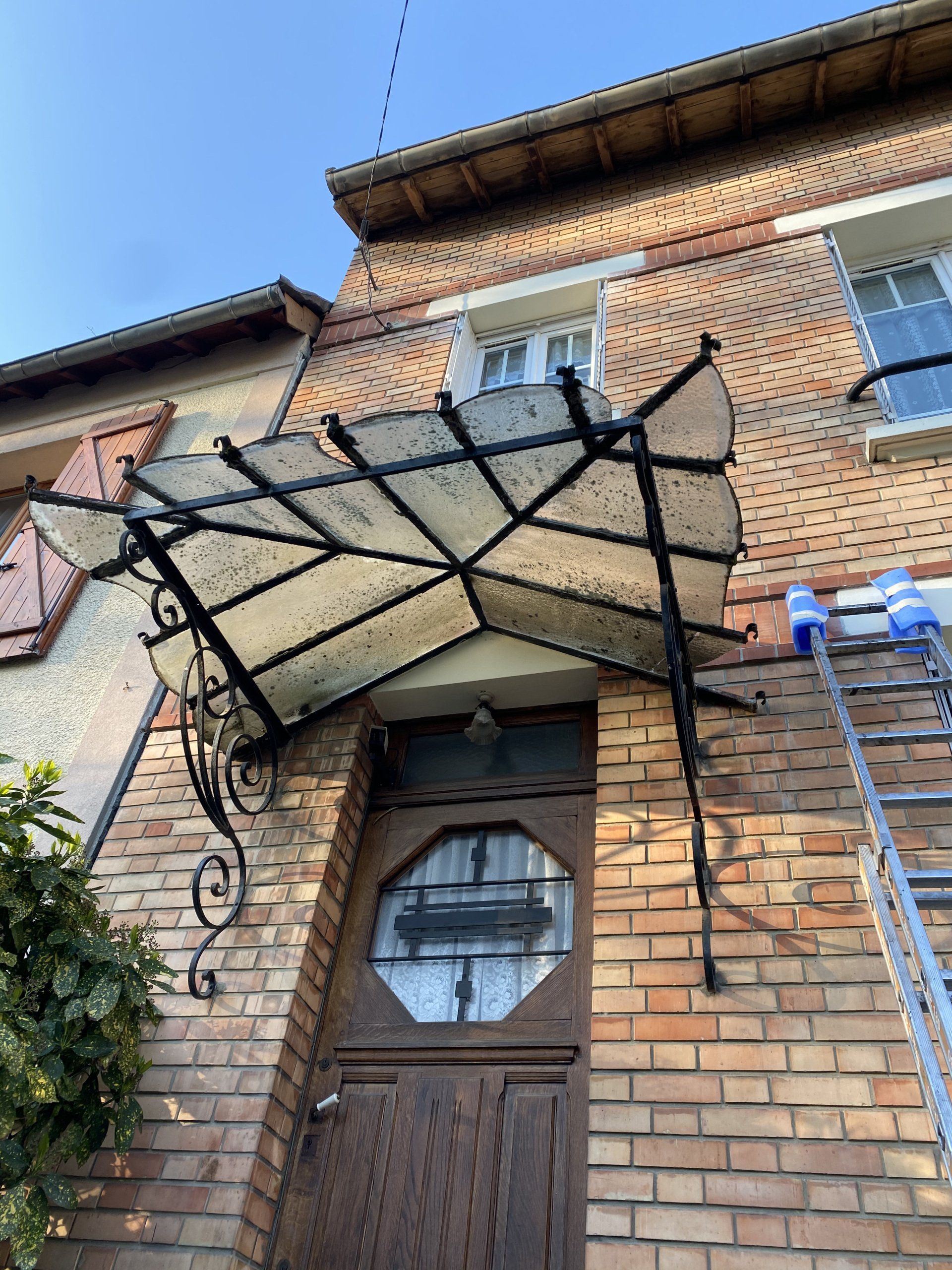 Bâtiment en briques avec une marquise en verre et en métal au-dessus d'une porte en bois. Une échelle est appuyée contre le bâtiment.