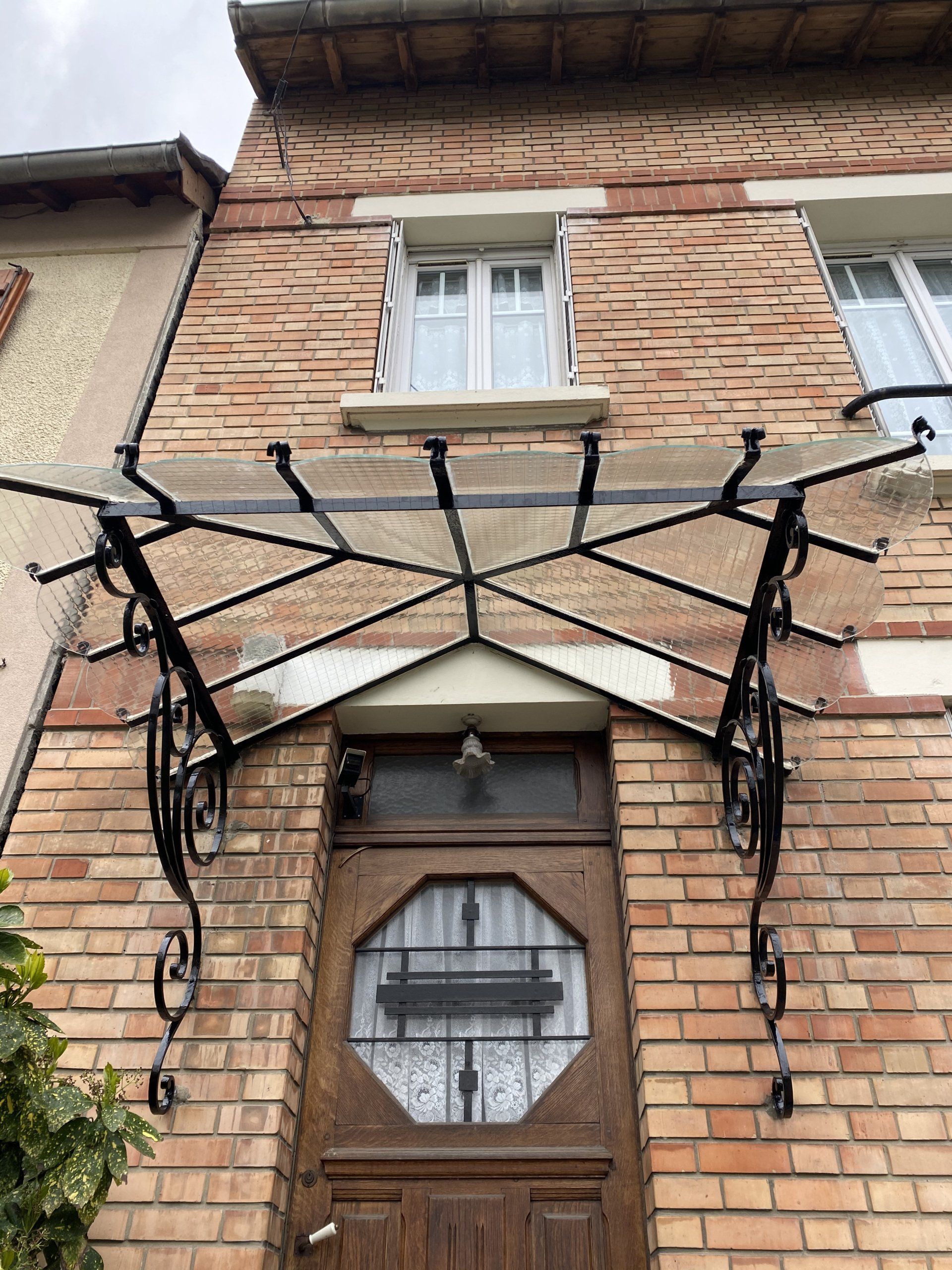 Maison en briques avec une porte en bois, surmontée d'une marquise en verre et métal noir.