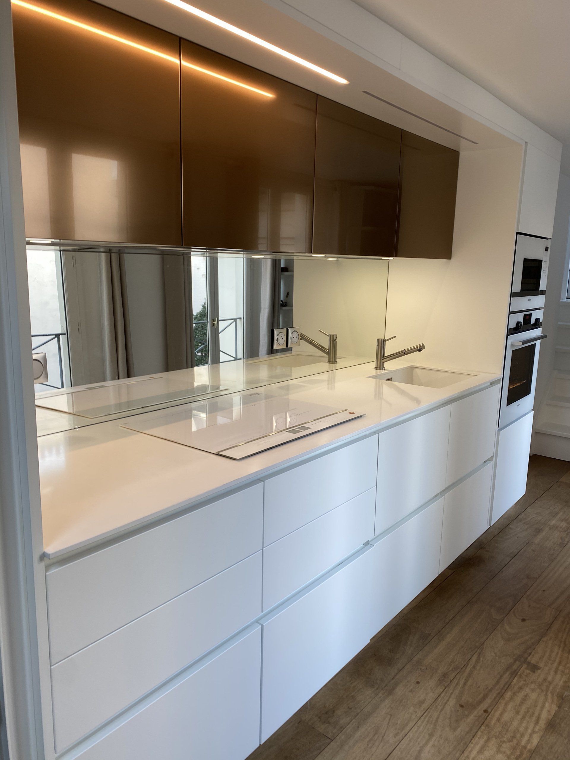 Cuisine moderne blanche avec placards hauts marron, comptoirs blancs et parquet.