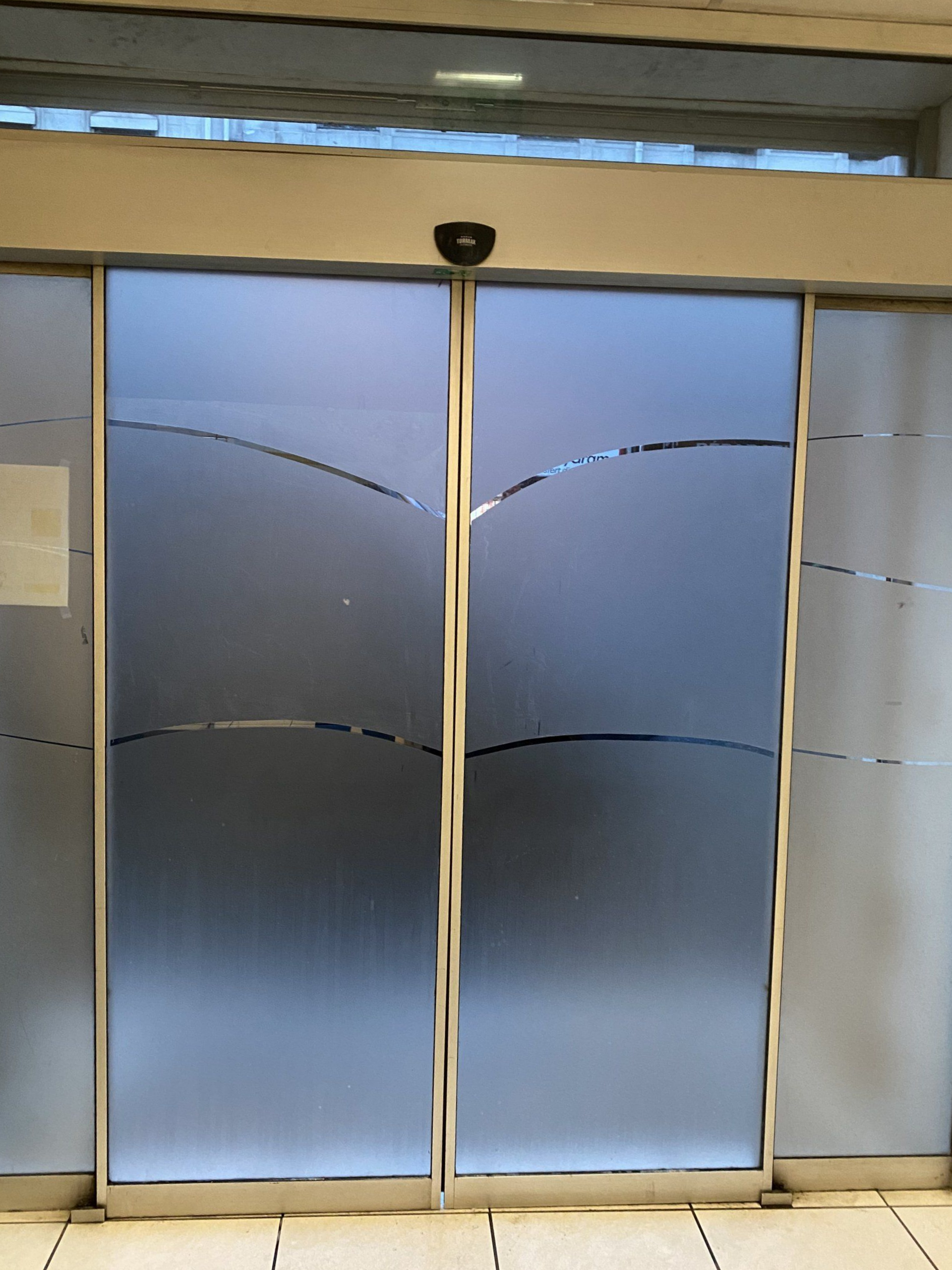 Portes coulissantes automatiques en verre avec panneaux en verre dépoli et lignes décoratives courbes.