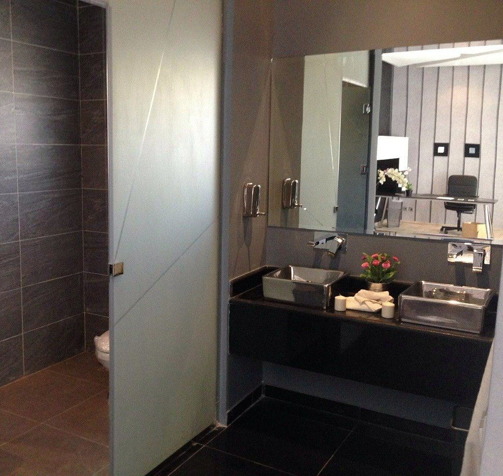 Salle de bains moderne avec meuble de lavabo noir, lavabos, miroir et porte en verre dépoli donnant sur les toilettes.