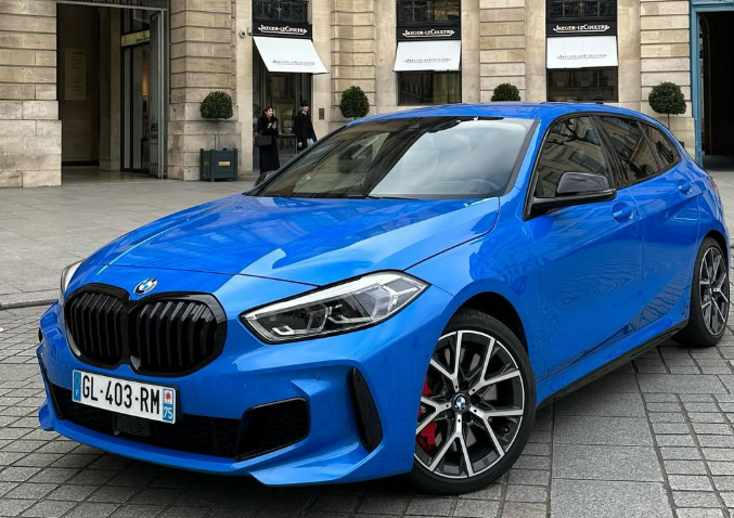 Une BMW bleue à hayon est garée dans une rue de la ville, devant un bâtiment.