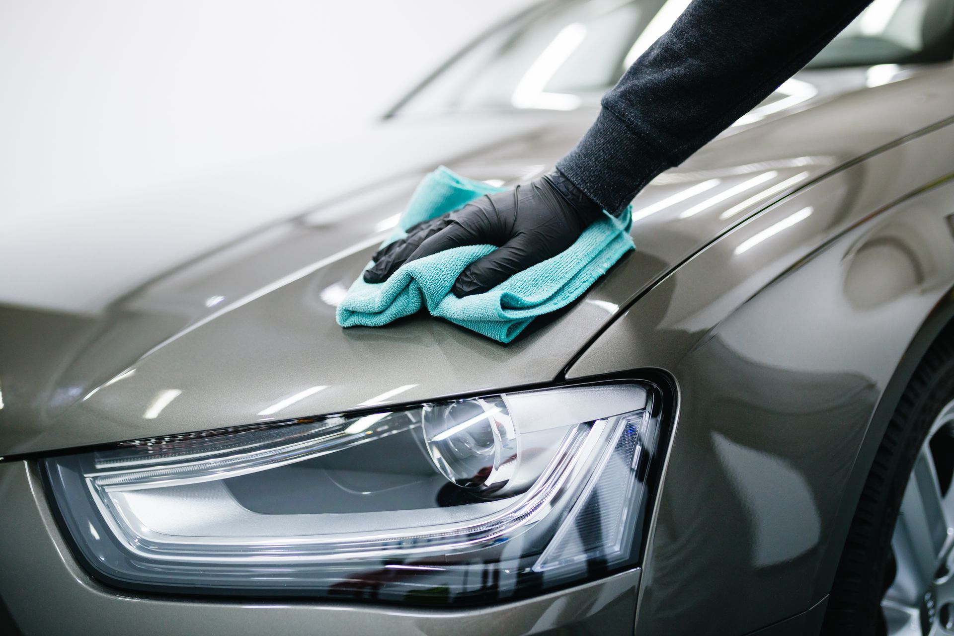 Une personne essuie le capot gris d'une voiture avec un chiffon turquoise pendant le nettoyage.