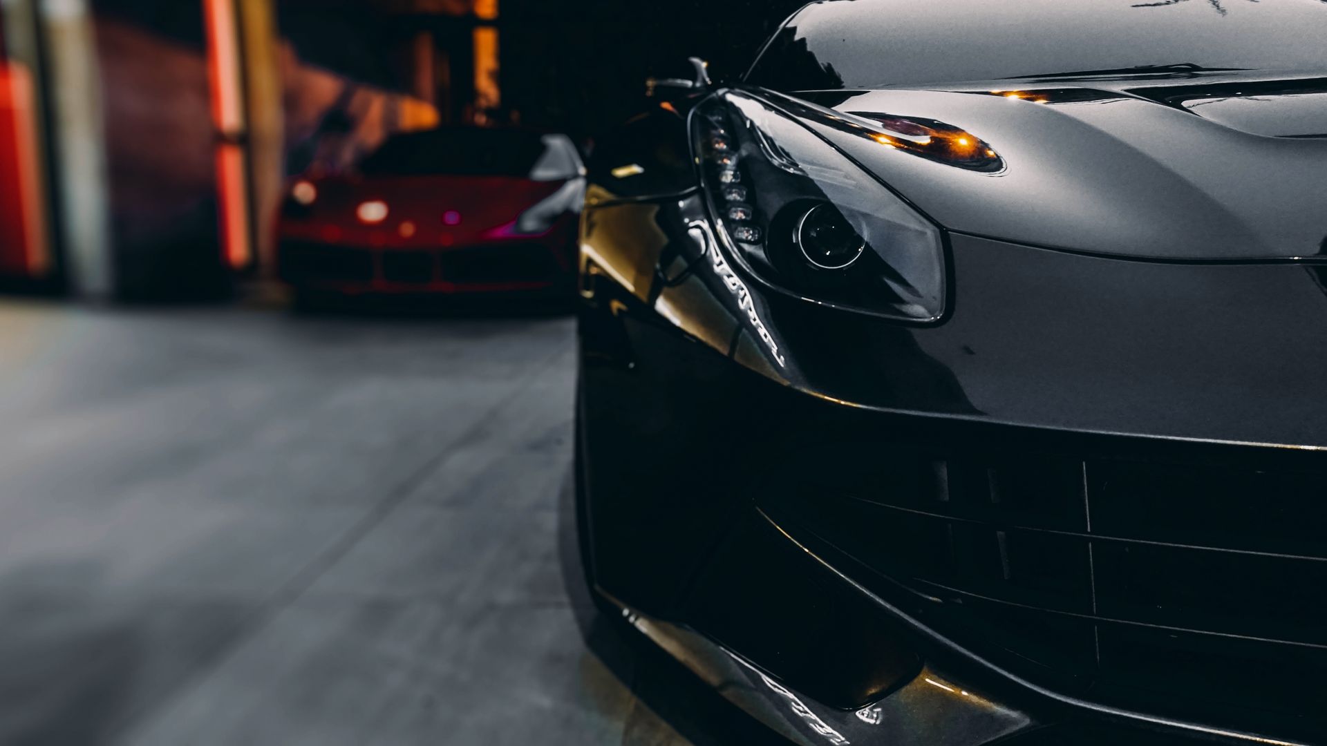 Gros plan sur une élégante voiture de sport noire dans un garage faiblement éclairé, avec une autre voiture floue en arrière-plan.