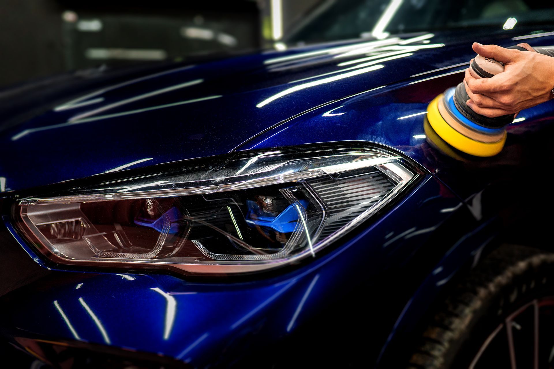 Polissage manuel du phare avant d'une voiture bleue à l'aide d'une polisseuse.