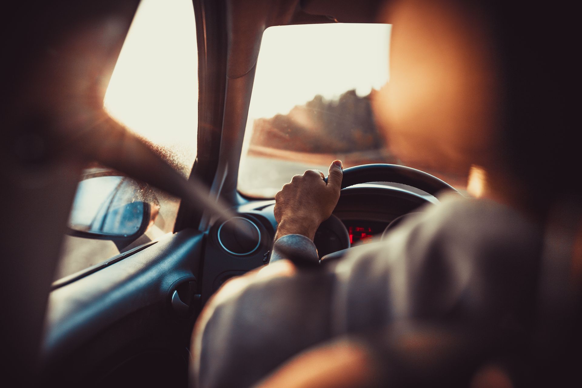 Les mains du conducteur sur le volant à l'intérieur d'une voiture, la lumière vive du soleil filtrant à travers le pare-brise.
