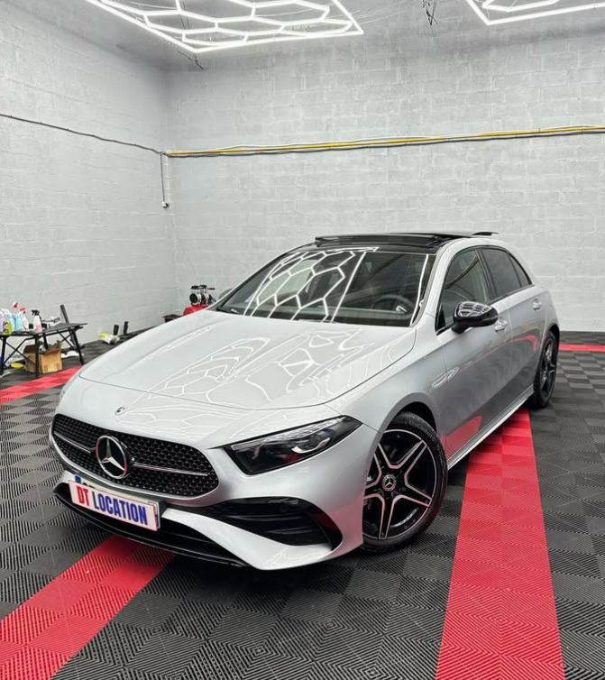 Berline Mercedes argentée dans un atelier de detailing avec tapis de sol noirs et rouges brillants et éclairage lumineux au plafond