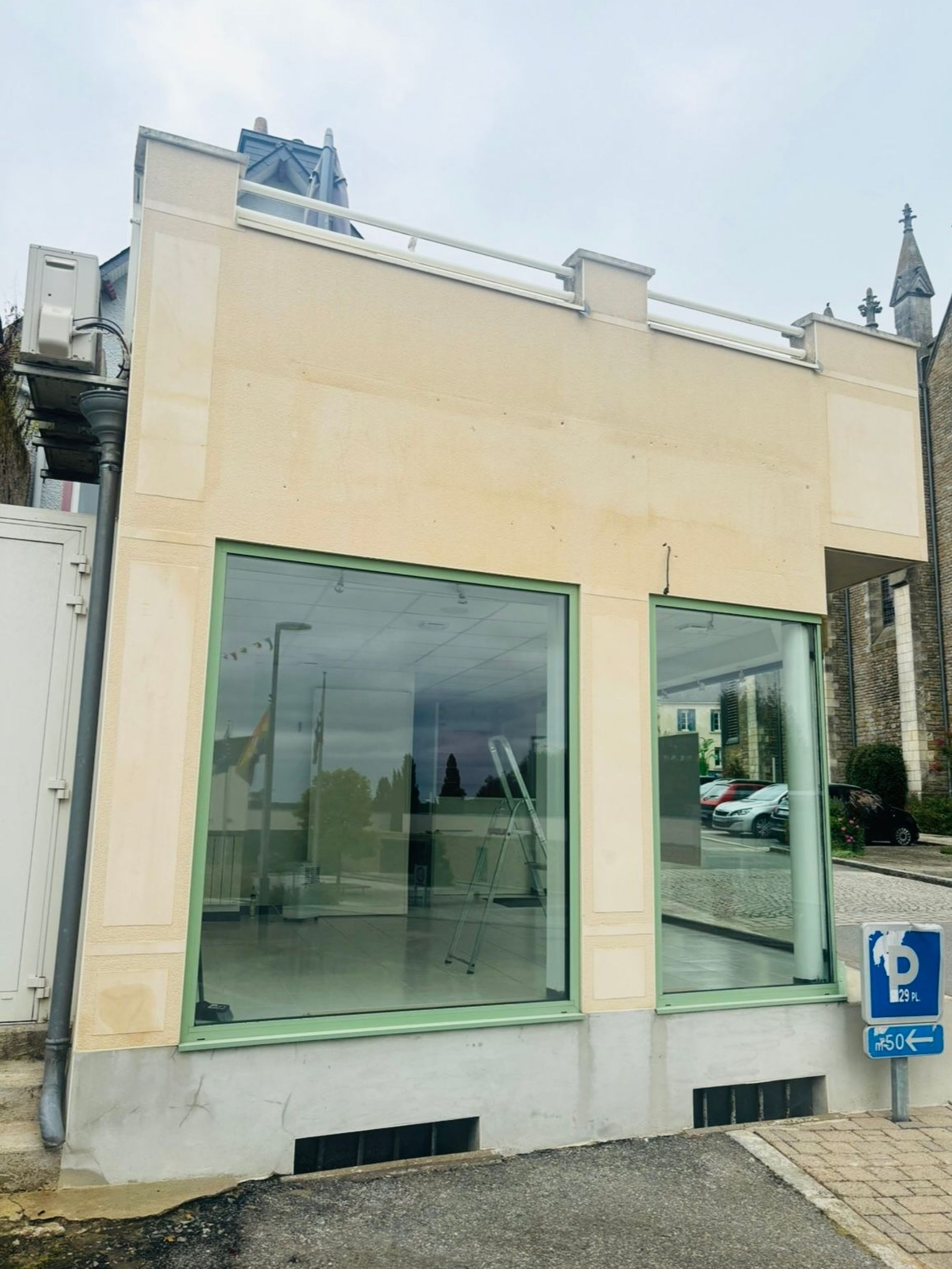 Une façade beige de plain-pied avec deux grandes vitrines, un toit plat et un panneau de stationnement sur la droite.