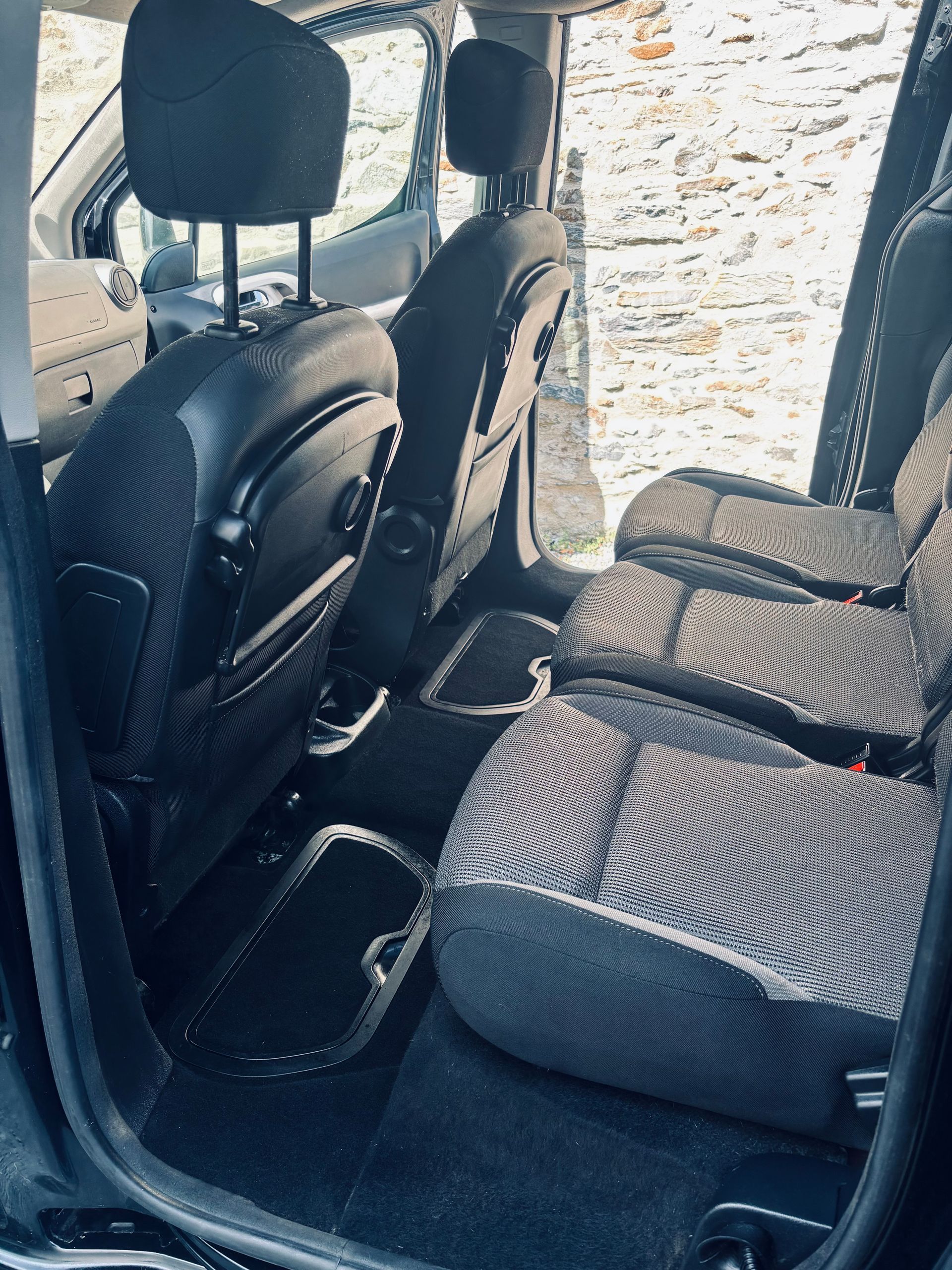 L'espace arrière d'un véhicule avec trois sièges individuels à motifs, une sellerie noire et des compartiments de rangement au sol.