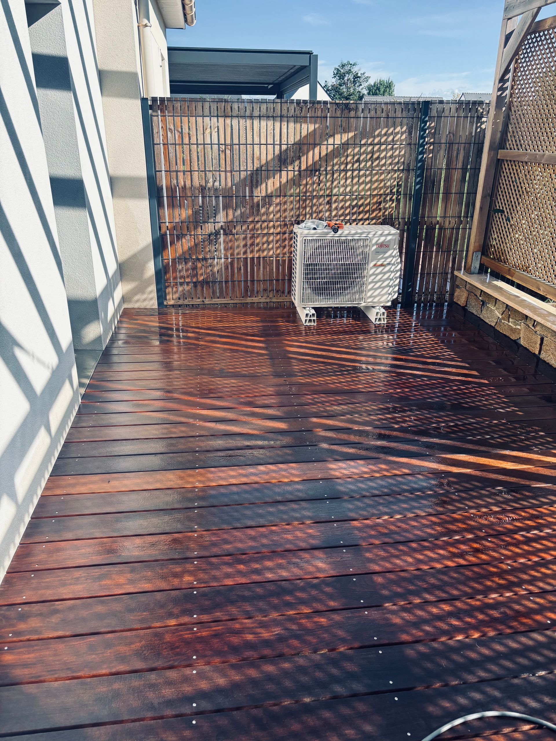 Terrasse en bois avec un climatiseur blanc et une clôture en bois pour préserver l'intimité, à côté d'une maison.