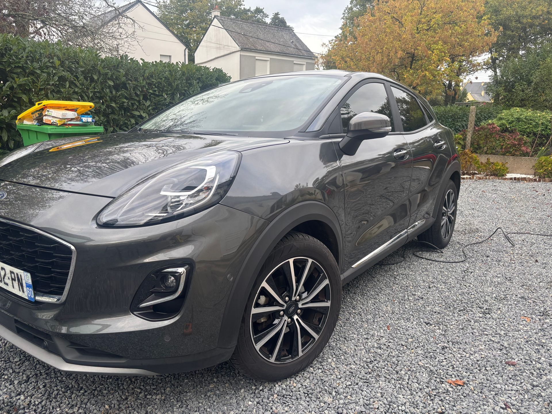 Un Ford Puma gris foncé, un crossover, est garé sur une allée de gravier devant une maison.