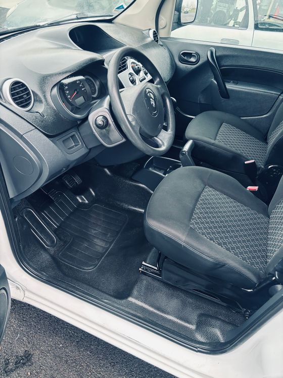 Vue intérieure d'une petite voiture stationnée montrant un volant, des sièges à motifs foncés et un tableau de bord noir.