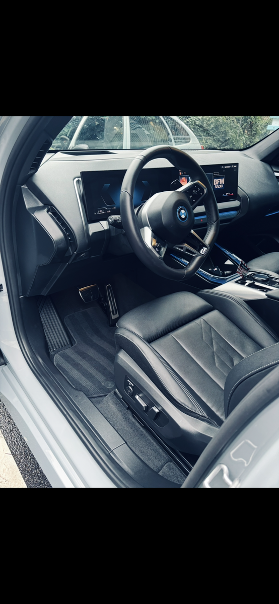 Intérieur de la voiture avec sièges, volant et tableau de bord noirs, vu depuis la porte conducteur ouverte