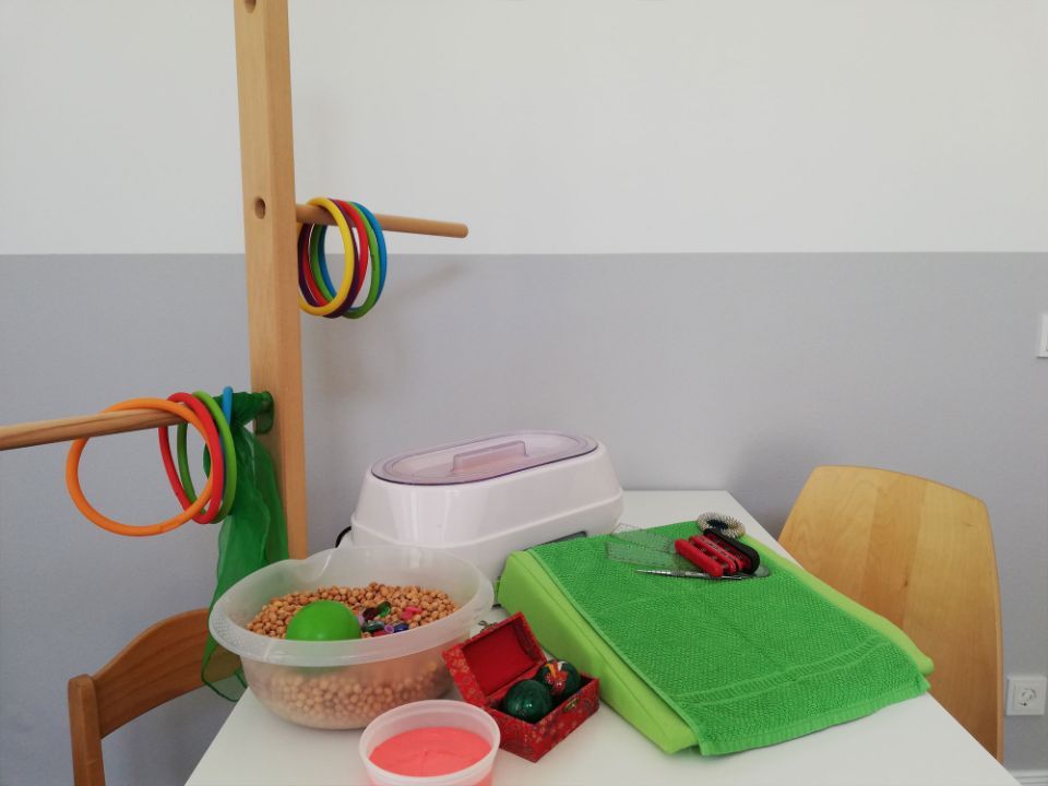 Ein Tisch mit Spielzeug und Zubehör, darunter ein Wachswärmer und ein Ringwurfspiel, vor einer grau-weißen Wand.