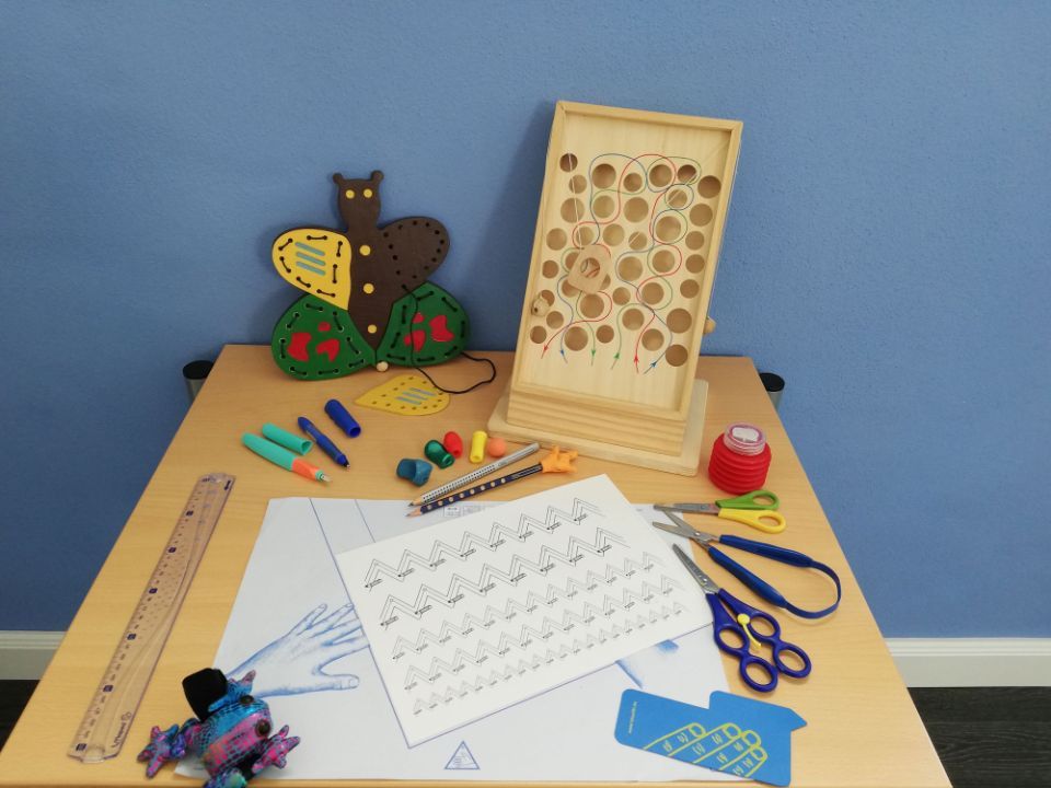 Bastelutensilien auf einem Tisch: Holzfädelspielzeug, Schere, Buntstifte, Papiervorlagen, Kunstwerk in Schmetterlingsform.