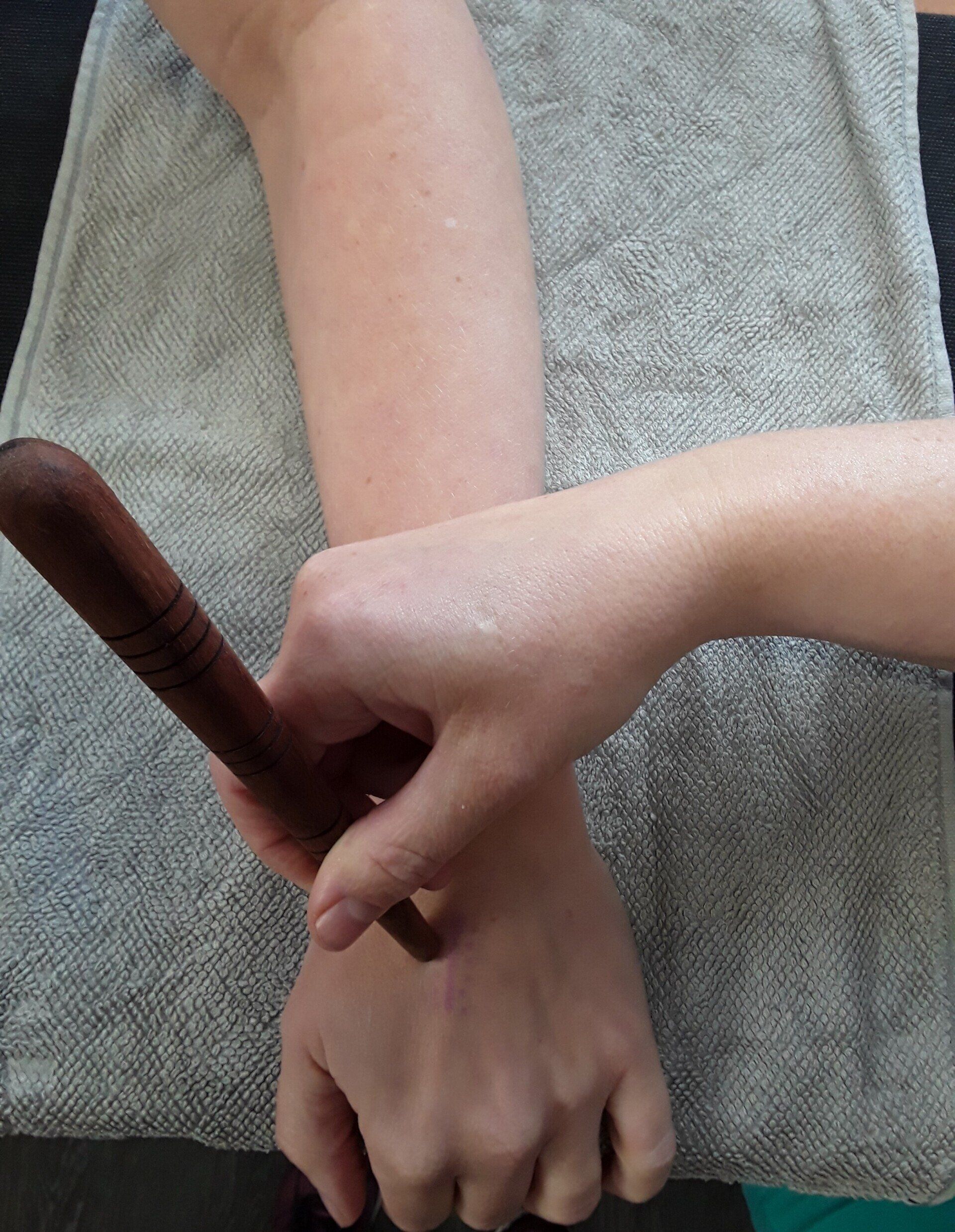 Person erhält Armmassage mit Holzwerkzeug; Hand hält Handgelenk.